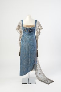 Vestido de noite de seda azul figurado com mangas de rede de ouro e trem bordado em faixa de metal ouro e decorado com pedras azuis e borlas, 1911 (seda)